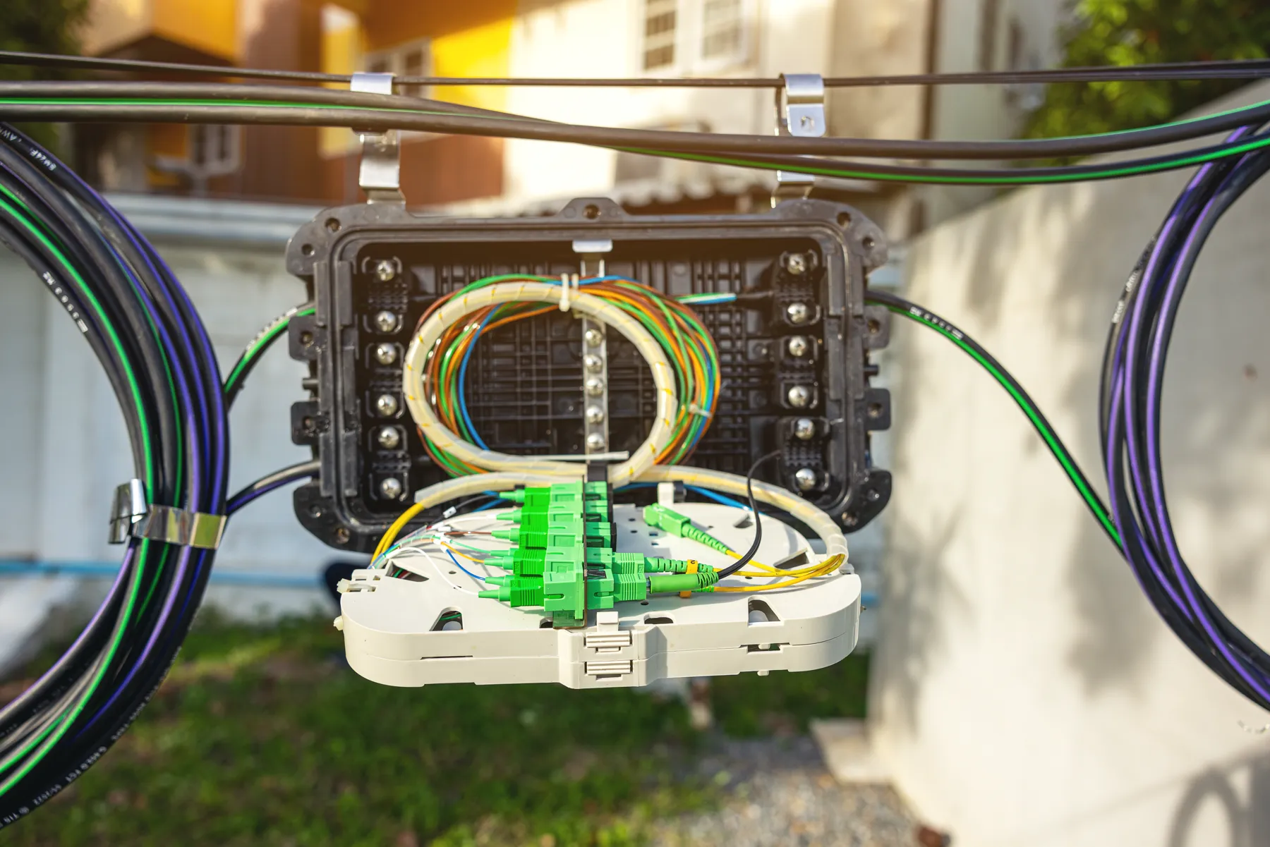 Fiber optic splice enclosure with green connectors on a line outside a house