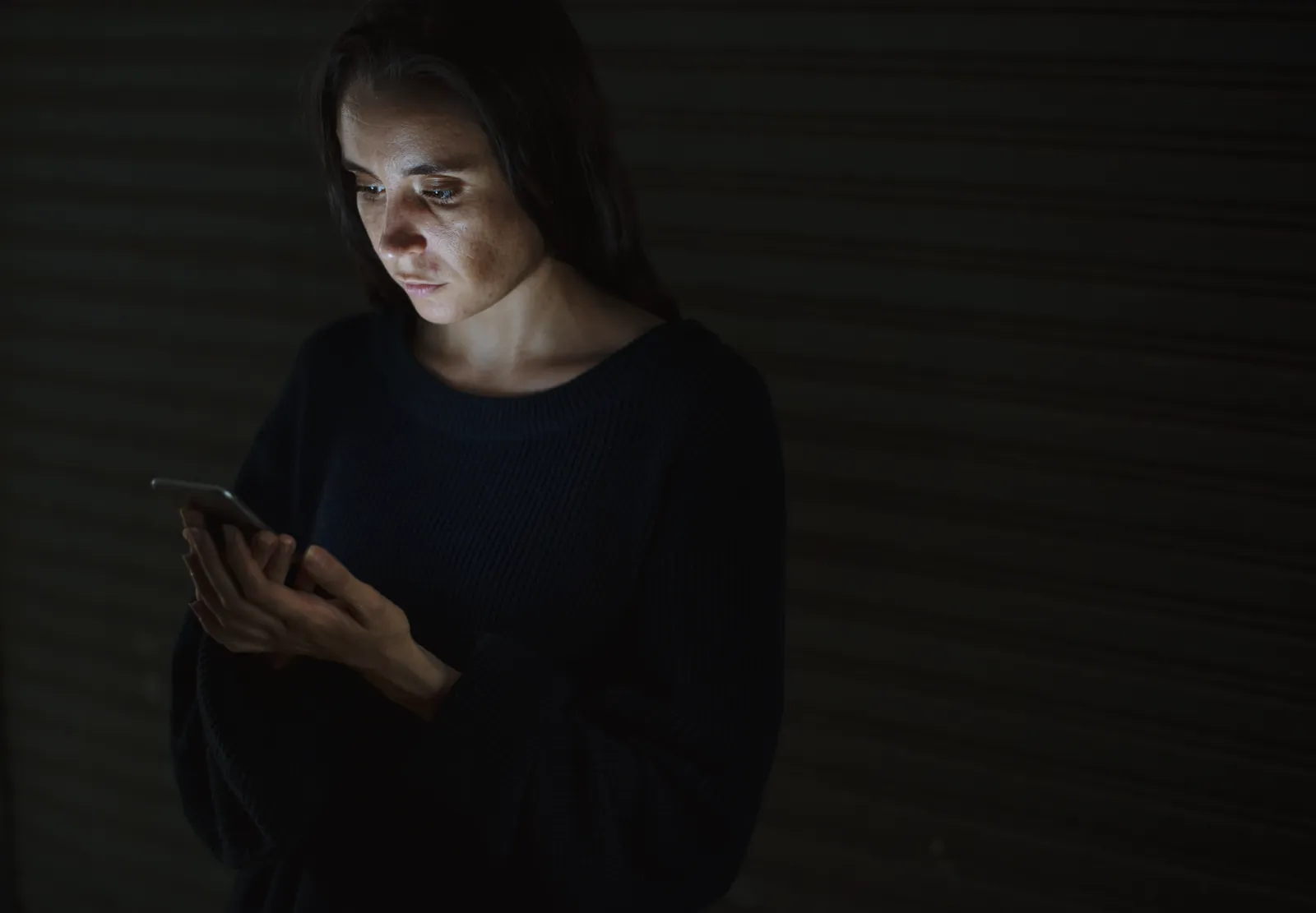 Woman reading her phone alone in a dark room