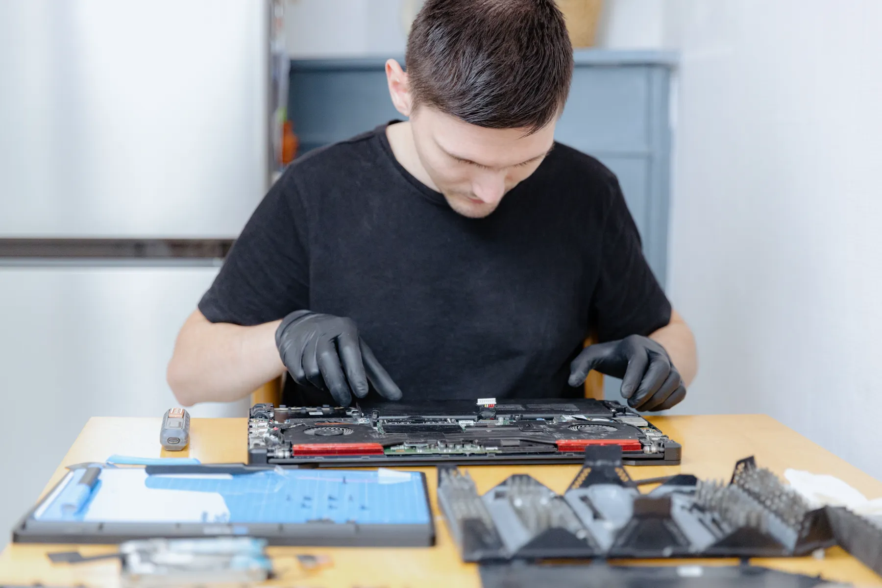 Technician in gloves working on an opened laptop at a repair bench